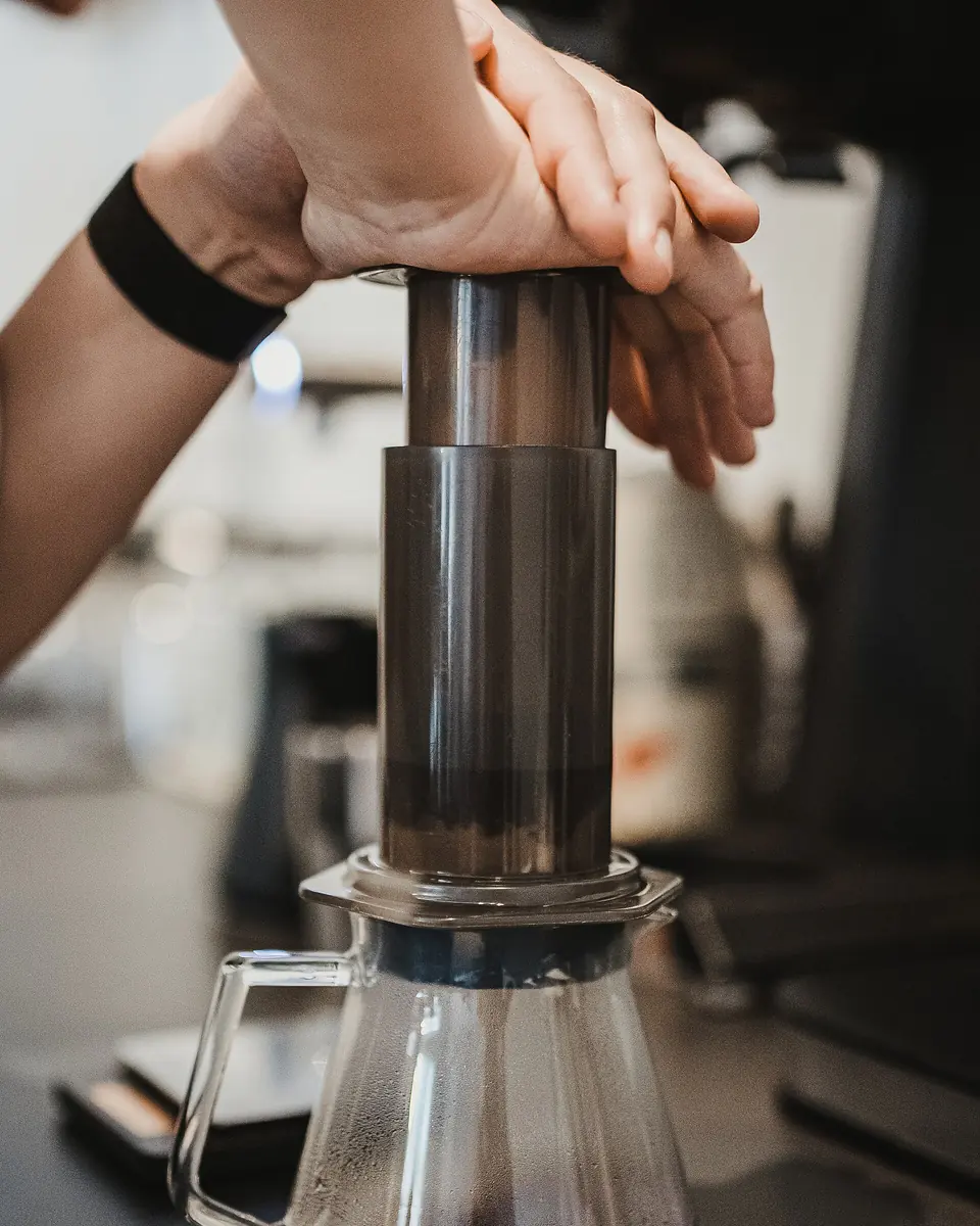 Two hands pressing an AeroPress plunger down into a glass carafe