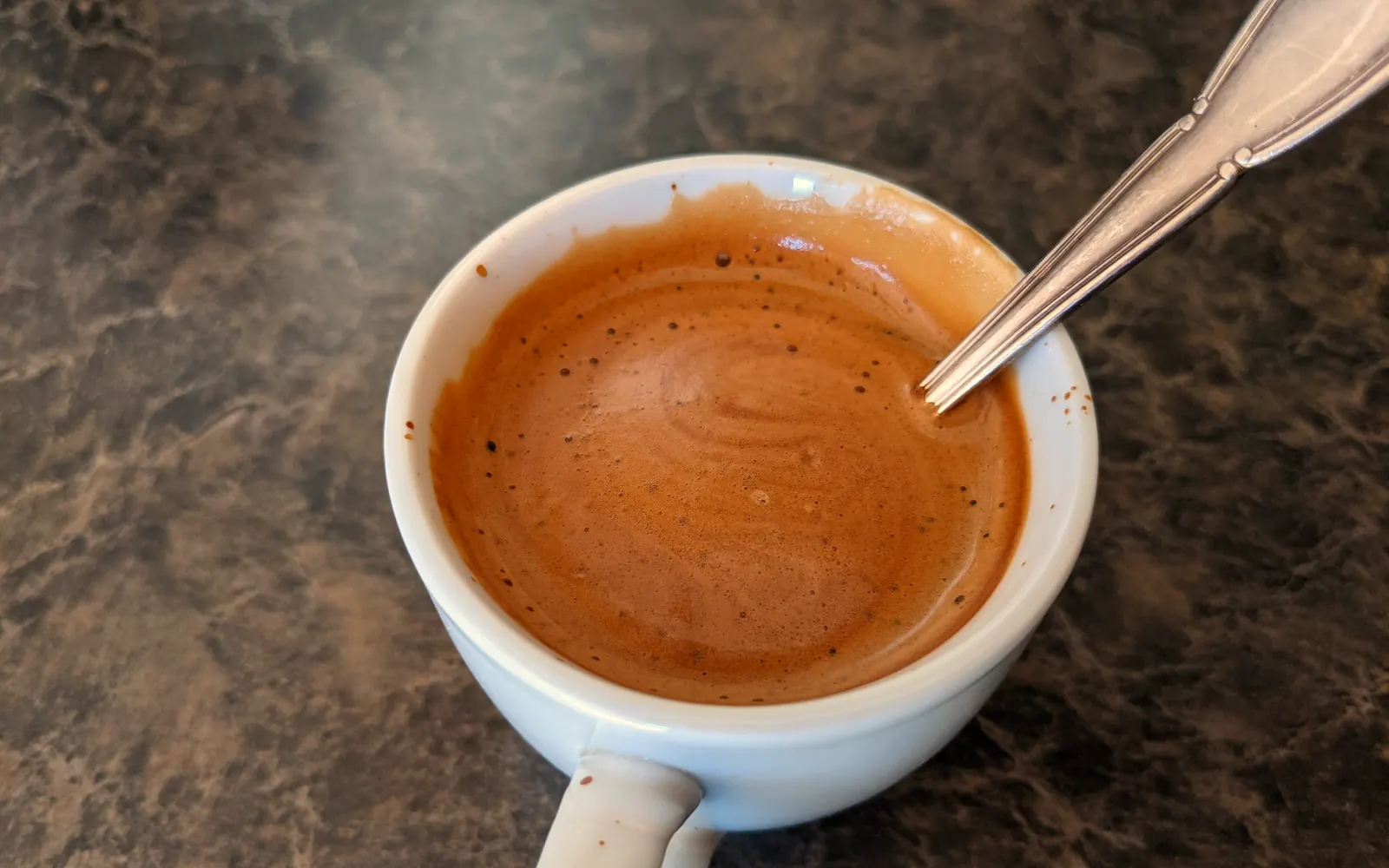 A double espresso in a white demitasse with a thick, tiger-striped golden crema