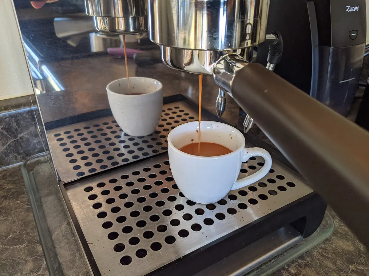 An espresso machine pulling a triple shot through a bottomless portafilter into a white cup
